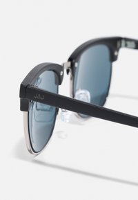 Schwarze Sonnenbrille mit kantigem Kunststoffrahmen, dunklen, getönten Gläsern und Metallelementen. Inklusive klarer Nasenpolster für Komfort und Stabilität.