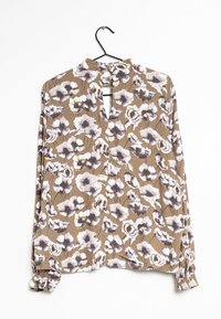 Brun blus med blommönster i lila och vitt. Har en nyckelhålsryg och långa ärmar med rynkade manschetter. Lättviktsmaterial.