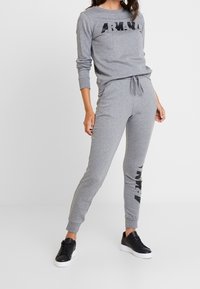 Conjunto de ropa de casa de algodón gris que incluye una camiseta de manga larga con un logotipo negro y joggers a juego con cintura ajustable y tobillos con puños. Zapatillas negras.
