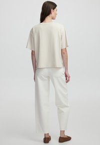 Top corto de manga corta en color crema con un corte suelto y aberturas laterales, combinado con pantalones blancos de tiro alto. Tejido suave con un diseño minimalista.