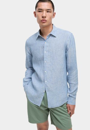 Lichtblauw overhemd met knopen, gemaakt van een gestructureerde stof, voorzien van een kraag en lange mouwen, gecombineerd met groene shorts.