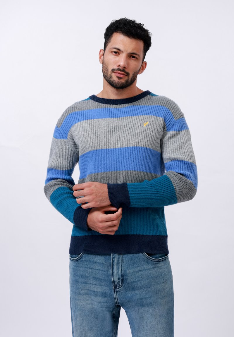 Jersey de punto a rayas en azul, gris y marino. Presenta una textura de canalé y un cuello redondo. Pequeño emblema en el pecho.