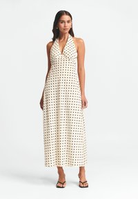 Vestido maxi en crema con lunares negros, diseño de cuello halter, cuerpo ajustado y falda fluida. Tejido suave y un look minimalista.