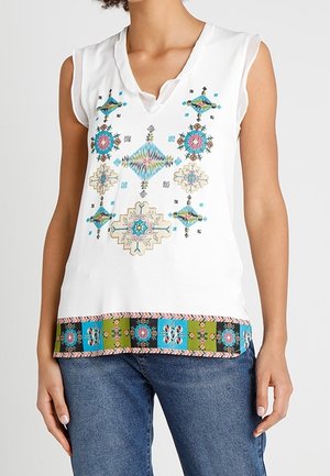 Top blanco sin mangas con bordado geométrico colorido en el frente y un dobladillo estampado, combinado con jeans azules.