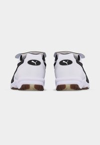 Pari valkoisia ja mustia Puma-tennareita nähtynä takaa, joissa on Puma-logot ja ruskeat kumipohjat yksivärisellä taustalla.