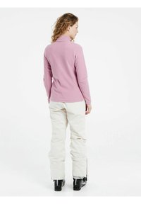 Top rosa chiaro a maniche lunghe con colletto alto, abbinato a pantaloni color crema con dettagli zip ai polsini e stivali neri.