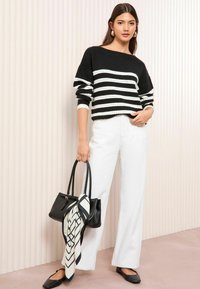 Maglione a righe bianche e nere con una vestibilità ampia e maniche over-size; abbinato a pantaloni bianchi a gamba larga e una borsa nera con una sciarpa decorativa.