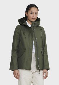 Veste imperméable vert olive avec capuche, cordons de serrage réglables, deux poches avant et fermeture éclair sur le devant. Texture de tissu lisse.