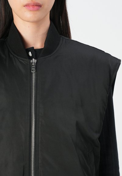 Giacca bomber senza maniche nera con colletto a coste, zip argento e tasche laterali. Texture liscia con linee pulite e senza motivi.