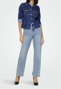 Jeansjacka med mörkblå tvätt, två bröstfickor och silverknappar, ihop med ljusblå raka jeans och svarta klackar.