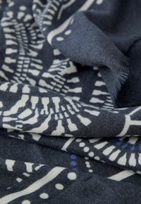 Navyblauwe stof met abstracte witte en blauwe patronen, met een zachte textuur en franjes aan de randen. Kreukelige, gelaagde uitstraling.