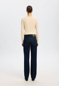 Helles Beige, langärmliges Rippoberteil kombiniert mit dunkelblauen, weit geschnittenen Jeans, die fünf Taschen und ein braunes Etikett am hinteren Taillenbund haben.