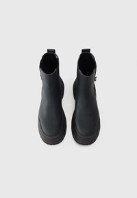 Botines de cuero negro hasta el tobillo con punta redonda, paneles elásticos laterales y suelas de goma texturizadas. Incluyen tiradores para un uso fácil.