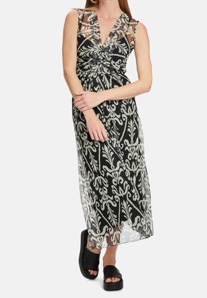 Kobieta w czarno-białej, bezrękawnikowej sukience maxi z dekoltem w serek i czarnych platformowych sandałach na płaskim obcasie, ze skrzyżowanymi rękami na talii.