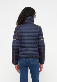 Marineblå pufferjakke med høj krave, horisontalt quiltet design og kontrasterende orange piping langs sømmene.