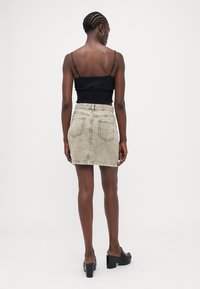 Black smocked top with thin straps, paired with a light beige denim mini skirt. Skirt features back pockets and a frayed hem. Black heeled mules.
