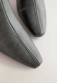 Szare skórzane botki za kostkę z wąskim czubkiem, teksturowanym wykończeniem, detalami szwów oraz gładką górną powierzchnią.