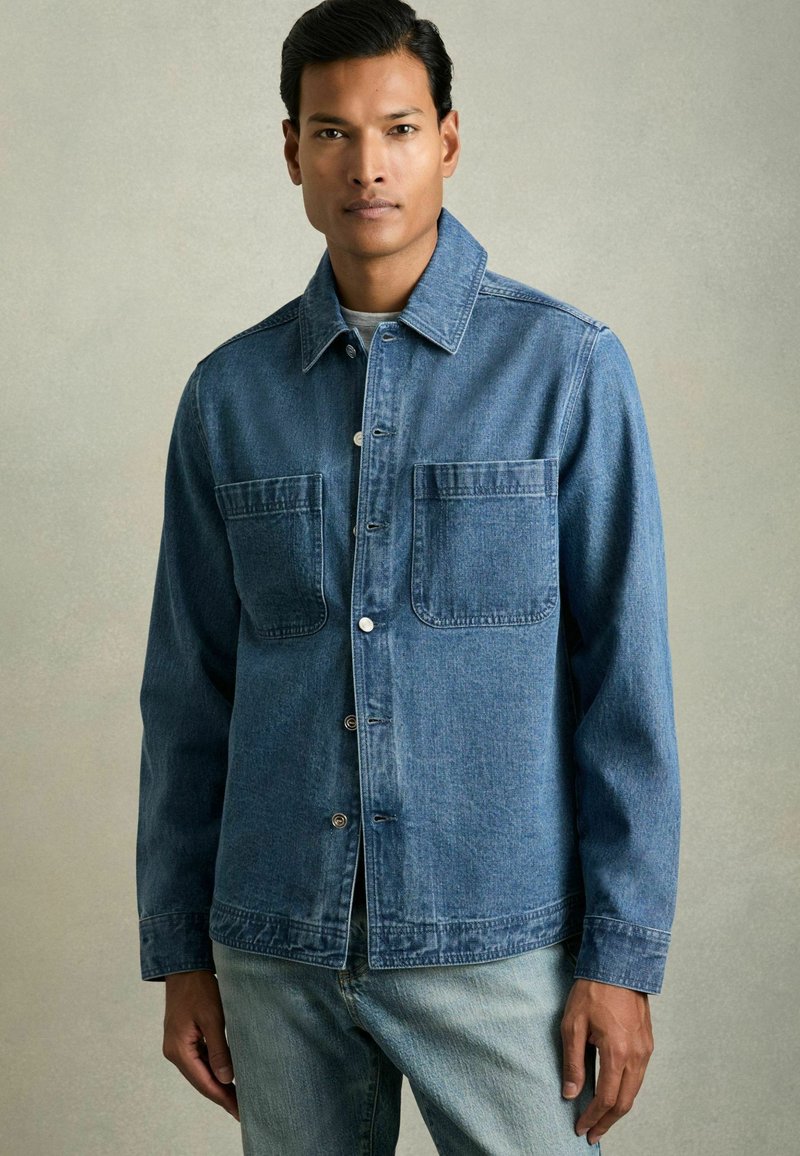 Jachetă din denim de culoare albastru mediu, cu închidere prin butoane, două buzunare mari la piept și o claviatură clasică. Textură ușoară, croi casual.