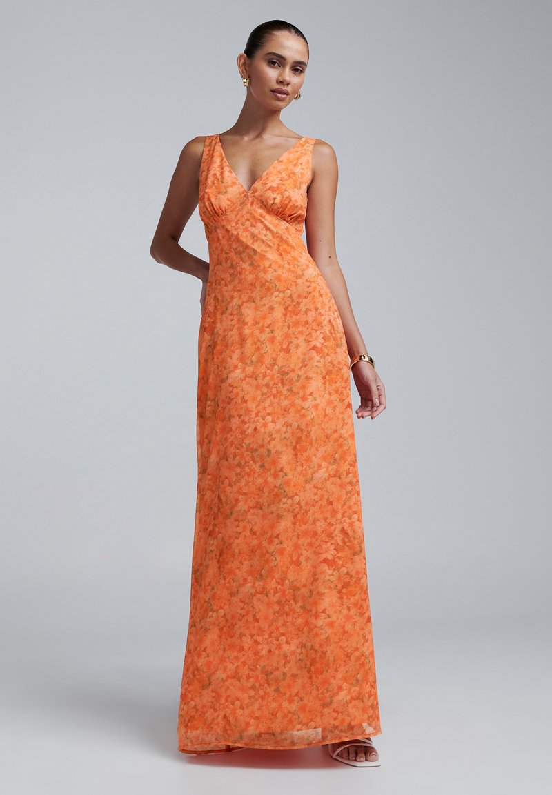 Maxi obleka v svetlo oranžni cvetlični vzorcu, z V-izrezom in prilegajočim pasom. Gladka tekstura, brez rokavov in tekoča krila.