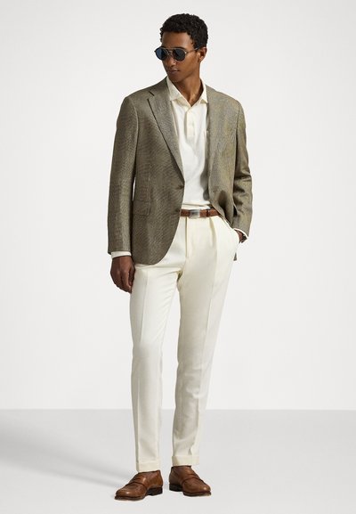 Blazer texturat maro peste un polo deschis, pantaloni crem și pantofi maro. Accesoriile includ ochelari de soare închiși la culoare și un curea maro.