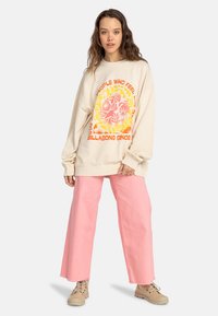 Beige oversized sweatshirt with vibrant floral print in pink and yellow. Paired with loose pink pants and beige lace-up shoes.