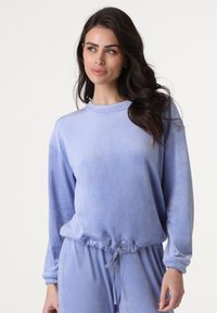 Top lungo a maniche di velluto viola chiaro con scollatura rotonda e vita arricciata. Vestibilità ampia con polsini a costine e dettaglio con coulisse.