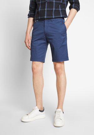 Chinos de algodón azul marino, hasta la rodilla, con dos bolsillos delanteros y un dobladillo limpio, combinados con zapatillas blancas con un acento azul marino.