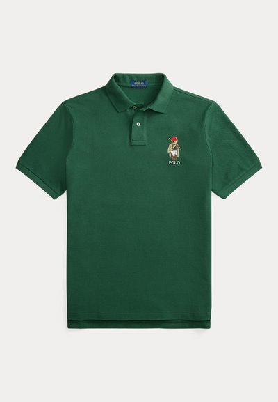 Temno zelena bombažna polo majica. Ima klasičen ovratnik, trojni gumb na sprednji strani in vezen logotip na levi strani prsnega koša. Kratki rokavi.