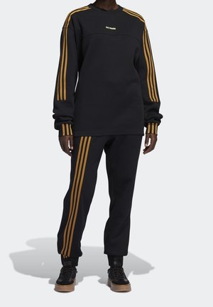 Ensemble sweat-shirt et pantalon noir avec des rayures verticales dorées et un logo brodé. Le sweat-shirt a un col rond ; le pantalon présente une coupe décontractée.