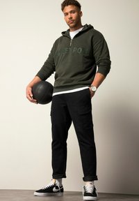 Olivengrüne Zip-up-Hoodie mit dem Text "STREET POET", schwarze Cargo-Hosen, ein schwarzer Basketball und schwarze Nike-Sneaker mit weißen Akzenten.