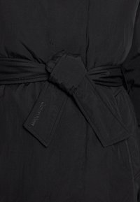 Svart ytterkläder med ett tygbälte med en rektangulär spänne. Den släta texturen och minimal sömnad framhäver dess moderna design.