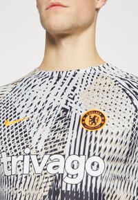 Nike football shirt featuring a mesh design in white, black, and beige, with orange logo accents and large "trivago" text.