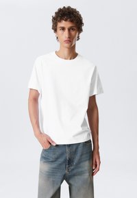 Weißes Baumwoll-T-Shirt mit rundem Halsausschnitt, kurzen Ärmeln und lockerer Passform, kombiniert mit hellblauen, leicht ausgebleichten Jeans.