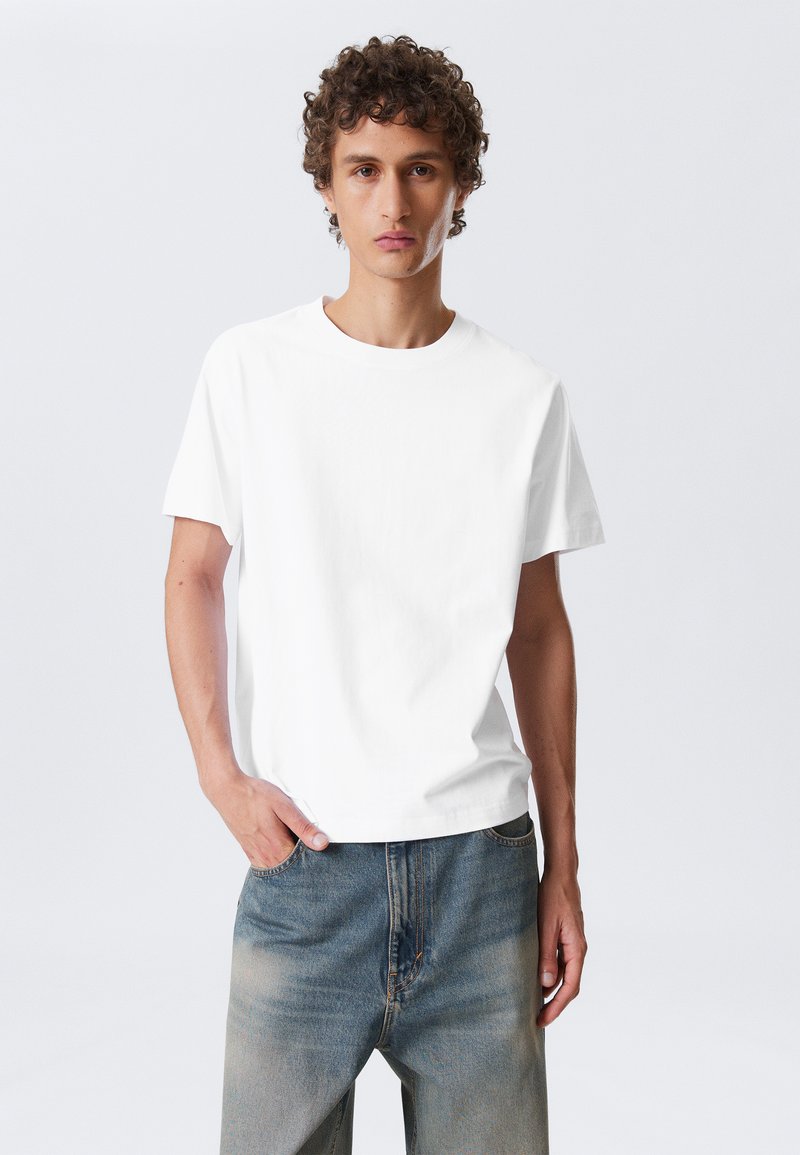 Weißes Baumwoll-T-Shirt mit rundem Halsausschnitt, kurzen Ärmeln und lockerer Passform, kombiniert mit hellblauen, leicht ausgebleichten Jeans.