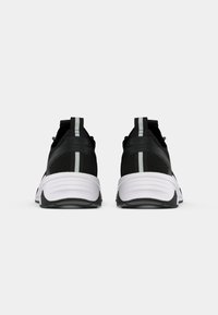 Black athletic shoes with a textured upper, featuring a white sole and grey accents. Includes a back pull tab and contrast stripe.