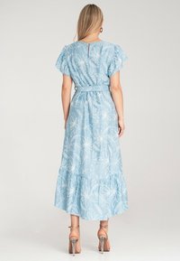 Jasnoniebieska maxi sukienka z haftem kwiatowym, falbaniaste rękawy, pasek do zawiązania w talii oraz spódnica w warstwach. Wysoki rozcięcie z tyłu.