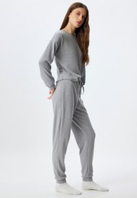 Set da salotto grigio con motivo testurizzato, maniche lunghe e cintura in vita. I pantaloni hanno una vestibilità rilassata e polsini a coste. Tessuto morbido.