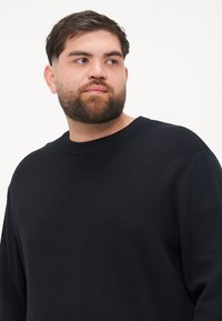 Pulover negru tricotat, cu guler rotund ribetat și mâneci lungi, având un material texturat și o croială lejeră.