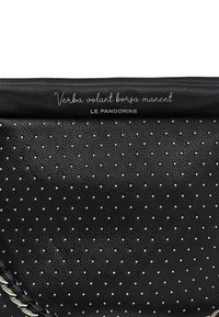 Borsa nera in pelle con motivo traforato e pois argentati, e tracolla intrecciata. Testo riportato: "Verba volant borsa manent, LE PANDORINE."