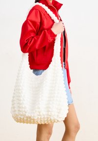 Vit texturerad tygväska med en mjuk, puffig design och ett brett handtag. Väskan har ett rynkat mönster, vilket ger ett rymligt inre.