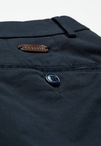 Ciemnoniebieska kieszeń spodni z czarnym guzikiem i małą brązową skórzaną metką przyszytą w pobliżu pasa.