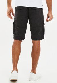 Shorts cargo noirs avec de multiples poches, coupe ample et détails de couture. Portés avec des baskets blanches ; présentent une texture lisse et mate.