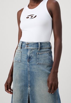 Femme portant un haut blanc sans manches avec détail découpé et une jupe en jean bleue avec poches avant et fermeture double bouton.