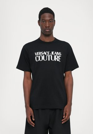 Juoda medvilninė marškinėliai su ryškiu baltu užrašu "VERSACE JEANS COUTURE." Standartinio kirpimo, trumpomis rankovėmis, apvali iškirptė. Paprastas dizainas.