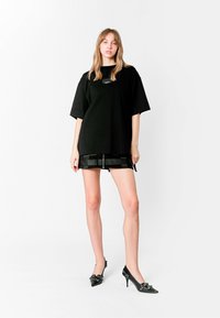 Camiseta negra de gran tamaño con corte recto, combinada con una mini falda negra de imitación cuero con detalles de cinturón y zapatos de tacón altos negros.
