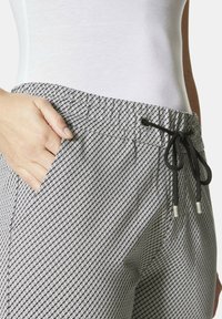Grau-weiße gemusterte Hose mit elastischem Bund, Kordelzugverschluss und Seitentasche. Strukturstoff mit geometrischem Design.