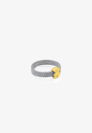 Anillo de malla plateada con un acento de diseño de conejo en tono dorado suave. La textura está tejida, creando una apariencia flexible y ligera.