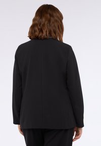 Sacou negru personalizat, cu o textură fină, umeri structurați, rever clasic și o deschidere singulară la spate, pentru un design ajustat.