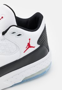 Bílé tenisky s černými akcenty a červeným logem Jumpman; mají texturovanou síťovinu, hladkou kůži a průhlednou modrou podrážku.