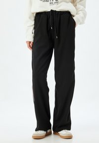 Pantalones de chándal negros con un corte relajado, cinturilla elástica, cordón ajustable y detalles de franjas laterales en colores contrastantes.